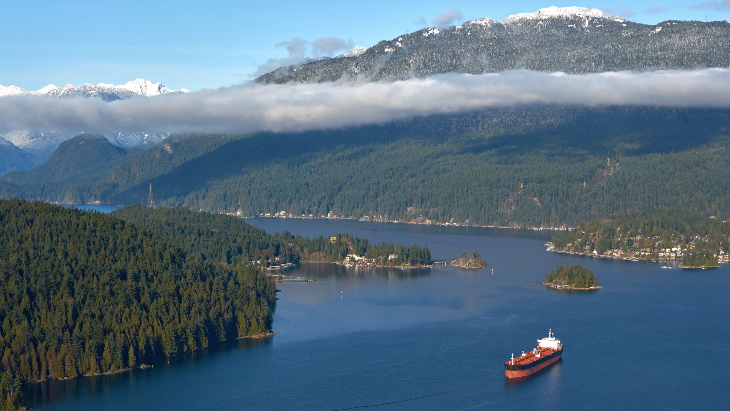 Large red oil tanker anchored in a picturesque bay surrounded by dense coniferous forest and snowy mountains